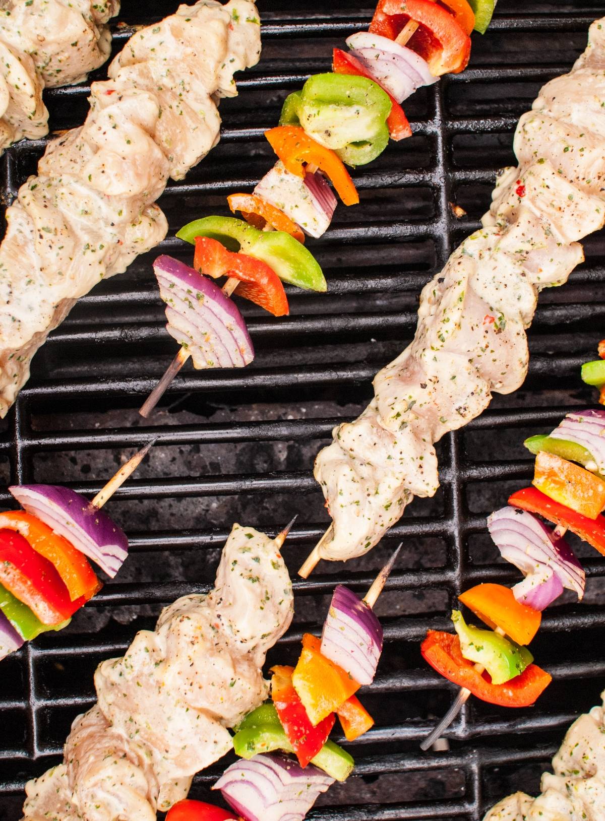 Raw Thai chicken skewers and fresh vegetables on a black grill, ready to be cooked and served with a savory cashew dipping sauce.