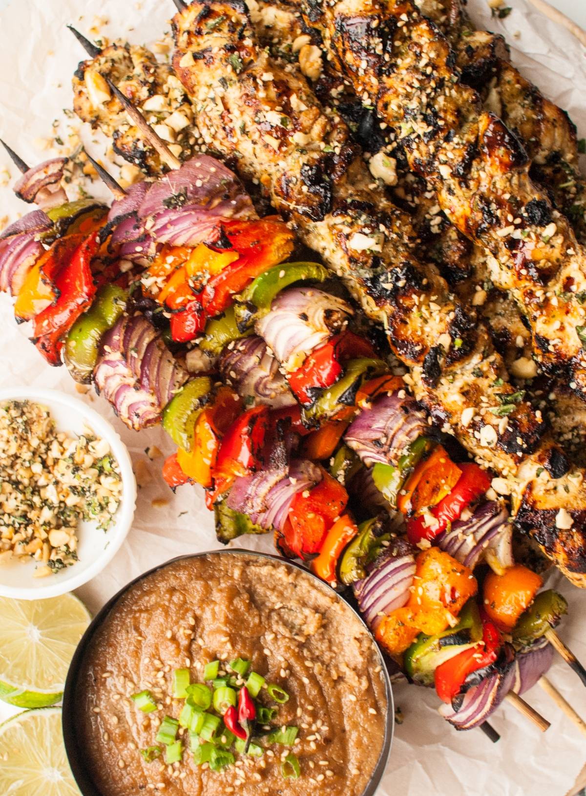 Grilled chicken and vegetable skewers with dairy free skewer marinade, served with cashew dipping sauce, chopped nuts, lime slices, and a fresh gremolata topping on a platter.