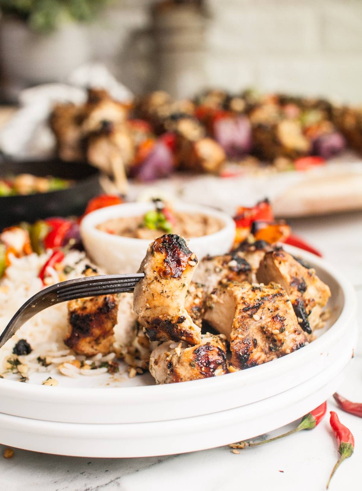 Grilled Thai Spicy Basil Chicken Skewers with rice and veggies on a white plate, served with a fork and cashew dipping sauce.