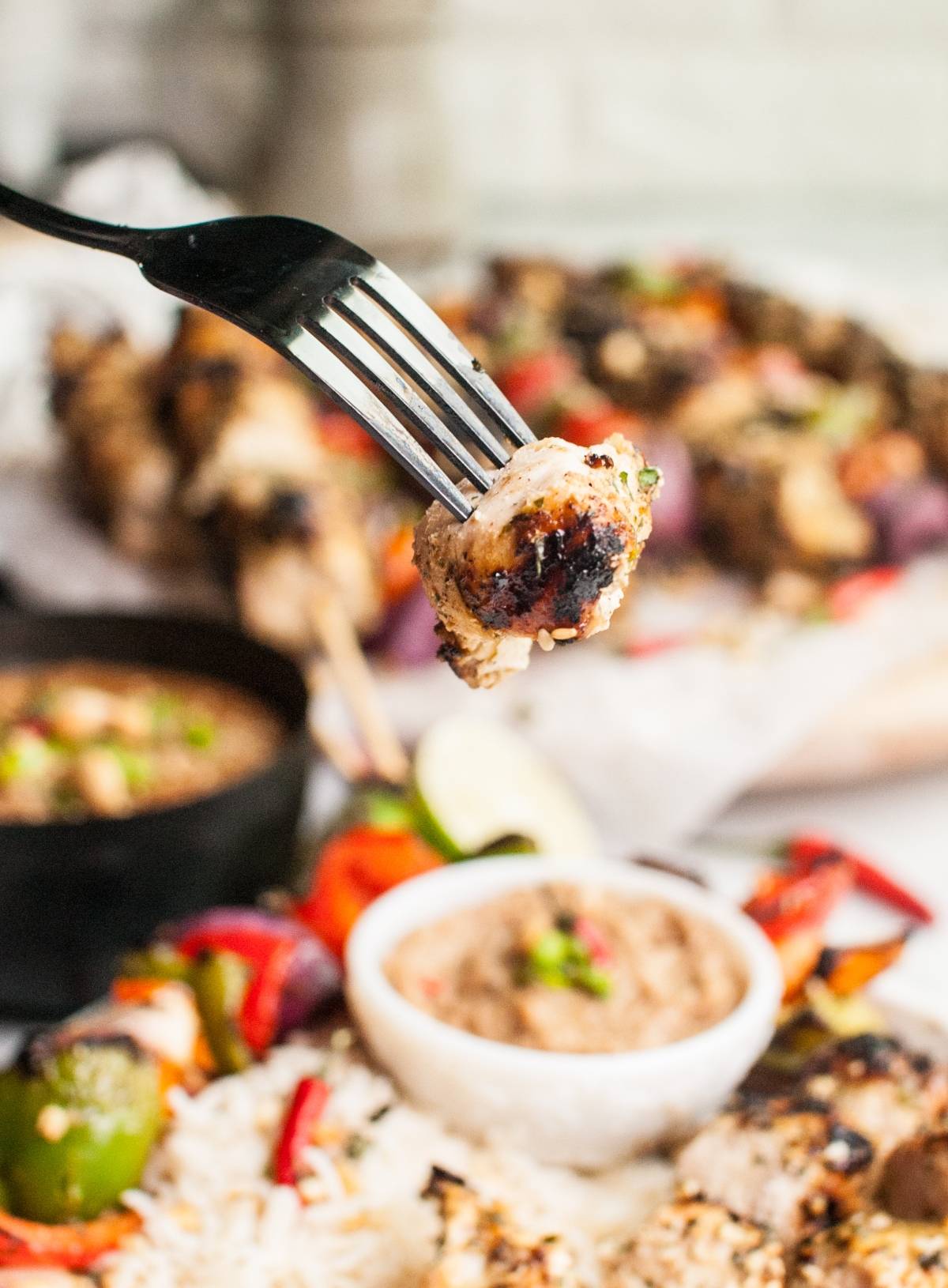 A fork holds Thai chicken skewers over a plate with rice, vegetables, and a bowl of dairy free skewer marinade for dipping.