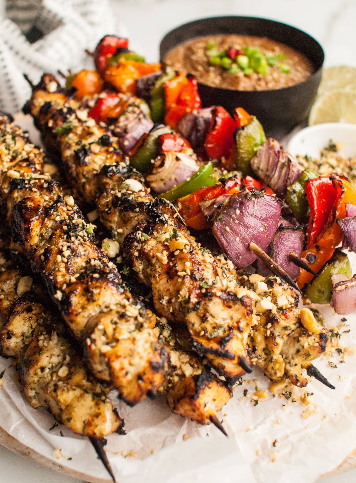 Grilled chicken and vegetable skewers with cashew dipping sauce on a plate, garnished with herbs, chopped nuts, and a zesty gremolata topping.