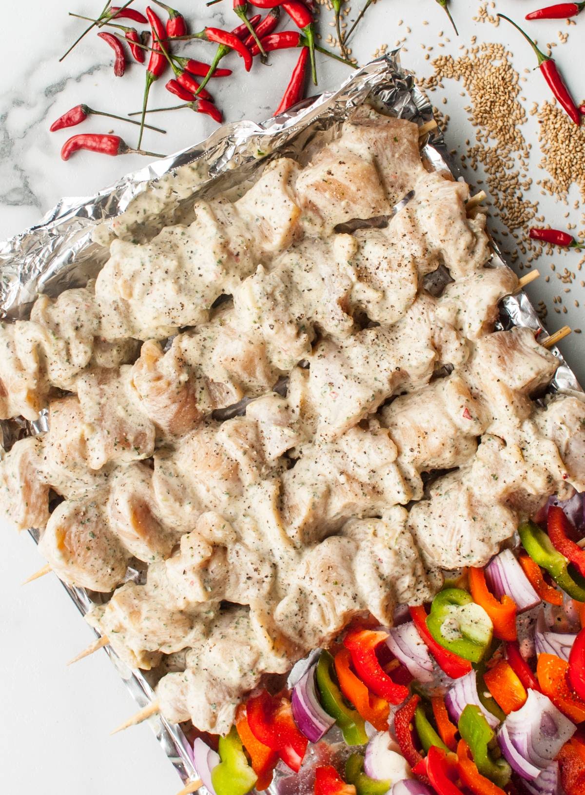 Skewers of marinated chicken and colorful sliced vegetables on a foil-lined tray, ready for grilling, served with a dairy free skewer marinade or zesty cashew dipping sauce.
