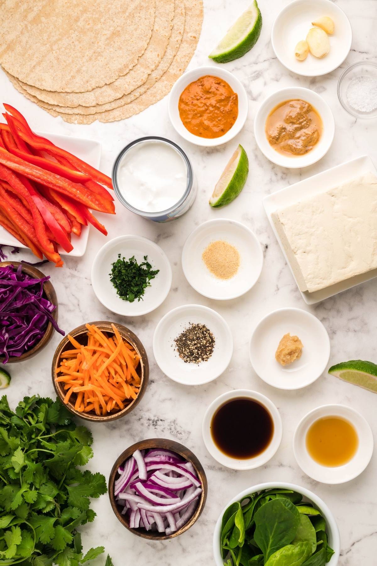 Assorted fresh vegetables, sauces, tofu, and seasonings arranged on a marble surface, ready for meal prep—perfect for a vegan gluten free lunch or an easy tofu wrap with Coconut Almond Butter Dip.