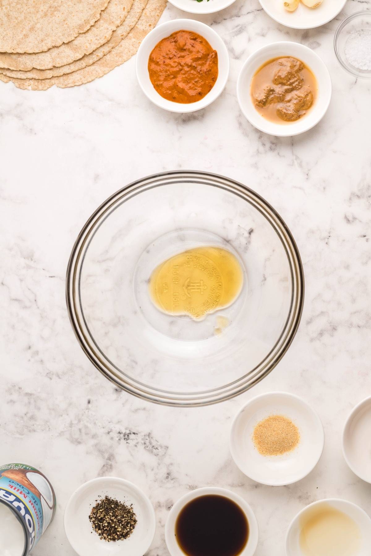 A glass bowl with Coconut Almond Butter Dip, surrounded by small bowls of spices, sauces, and tortillas—perfect for a Vegan Gluten free lunch on a marble surface.