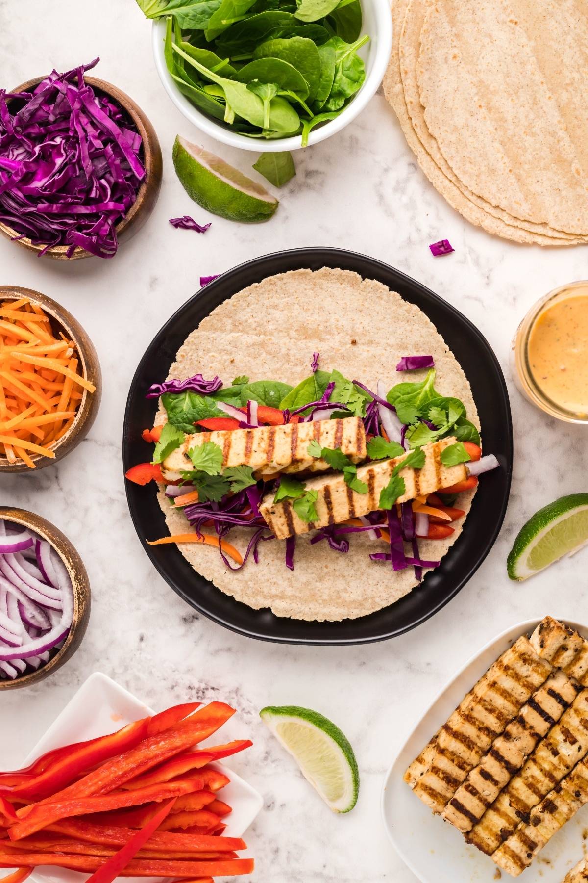 Open tortilla topped with grilled tofu, fresh spinach, shredded carrots, cabbage, red onion, and cilantro—enjoy as a Tofu Thai Wrap or pair with Coconut Almond Butter Dip for a delicious vegan gluten free lunch.