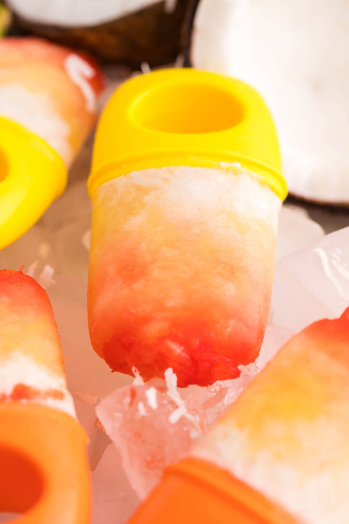 A close-up of colorful homemade sugar free popsicles with yellow and orange handles resting on ice, showcasing a vibrant layered popsicle recipe perfect for summer.