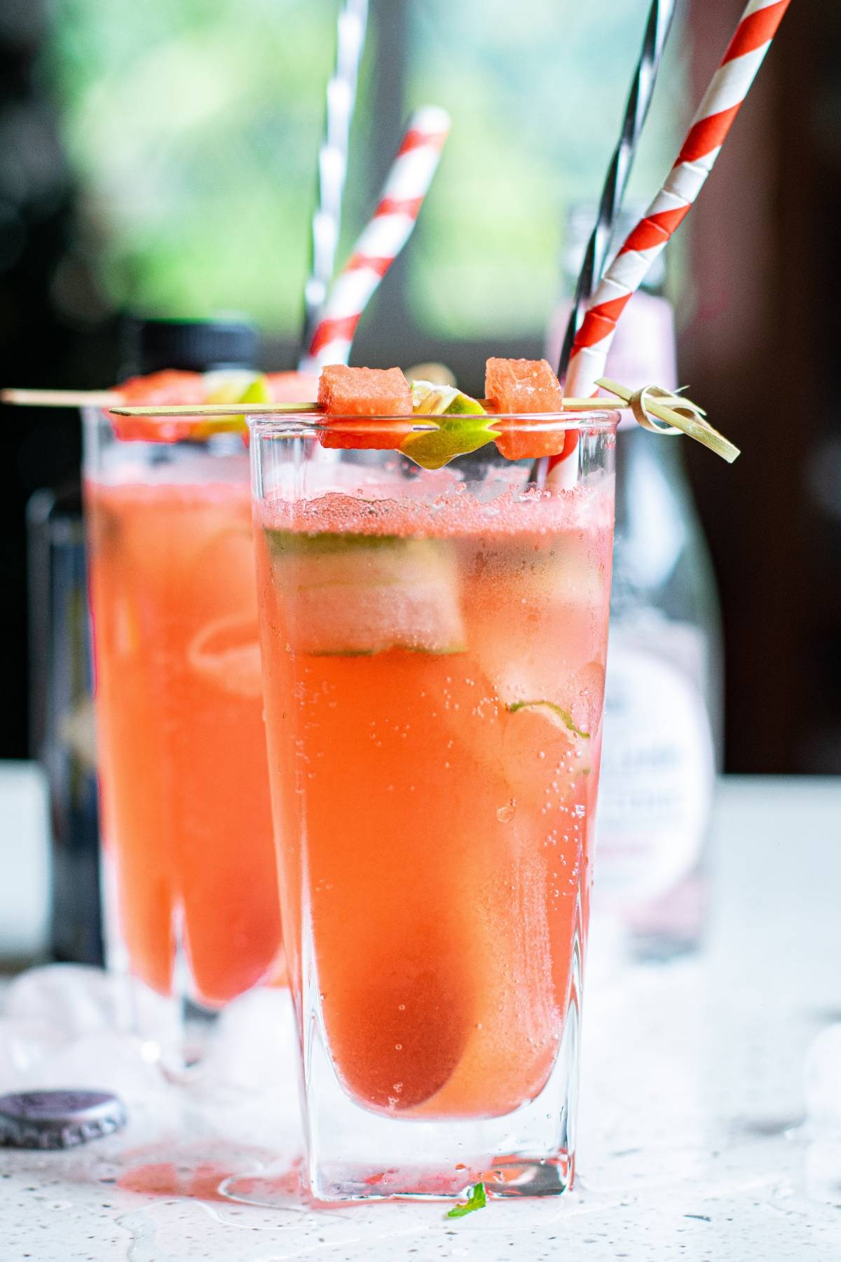 Two tall glasses of pink watermelon cucumber drink with ice, garnished with watermelon cubes and striped straws.