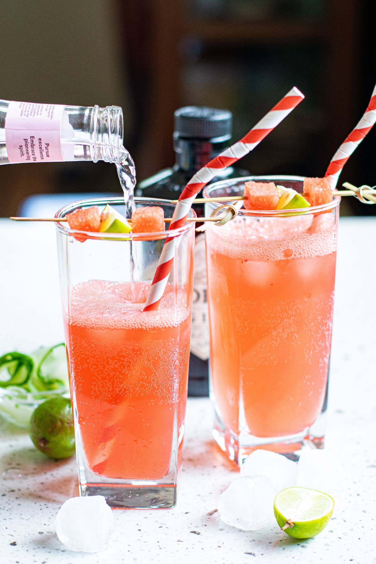 Two tall glasses of Watermelon Gin Tonic with striped straws, garnished with lime and watermelon cubes—a refreshing summer BBQ cocktail perfect for warm days.