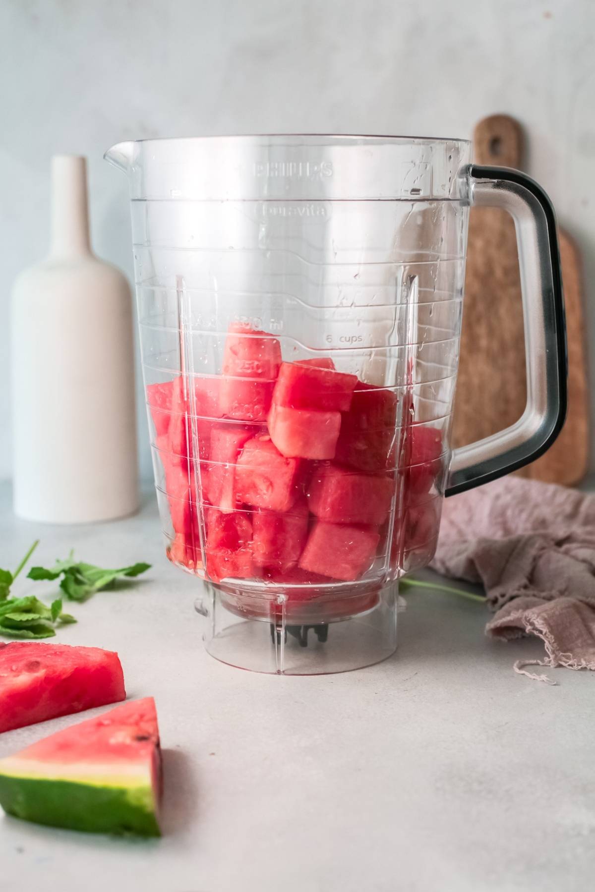 Blender pitcher filled with cubed watermelon on a kitchen counter, ready for a refreshing Watermelon White Wine Slushie recipe, with sliced watermelon nearby.