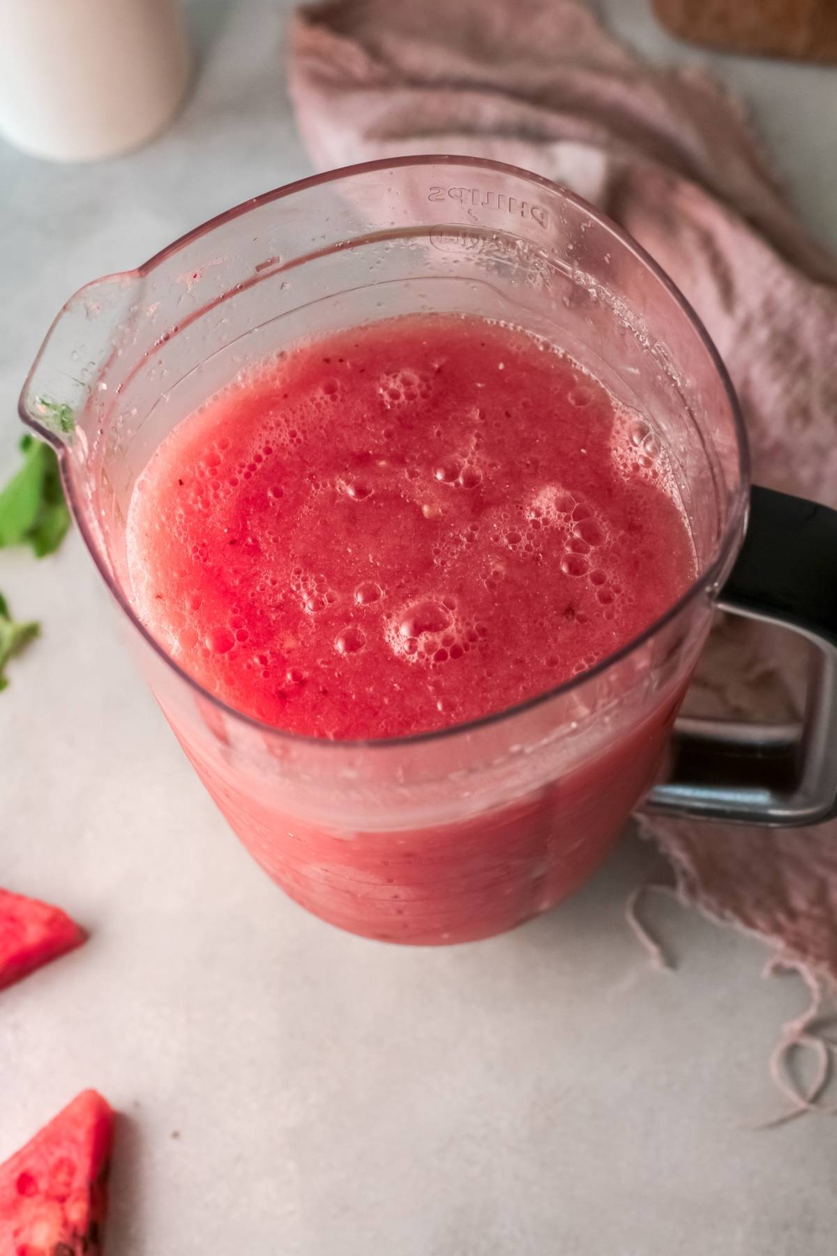 A blender pitcher filled with freshly blended Watermelon White Wine Slushie sits on a light countertop, perfect for an easy alcoholic slushie drink recipe.