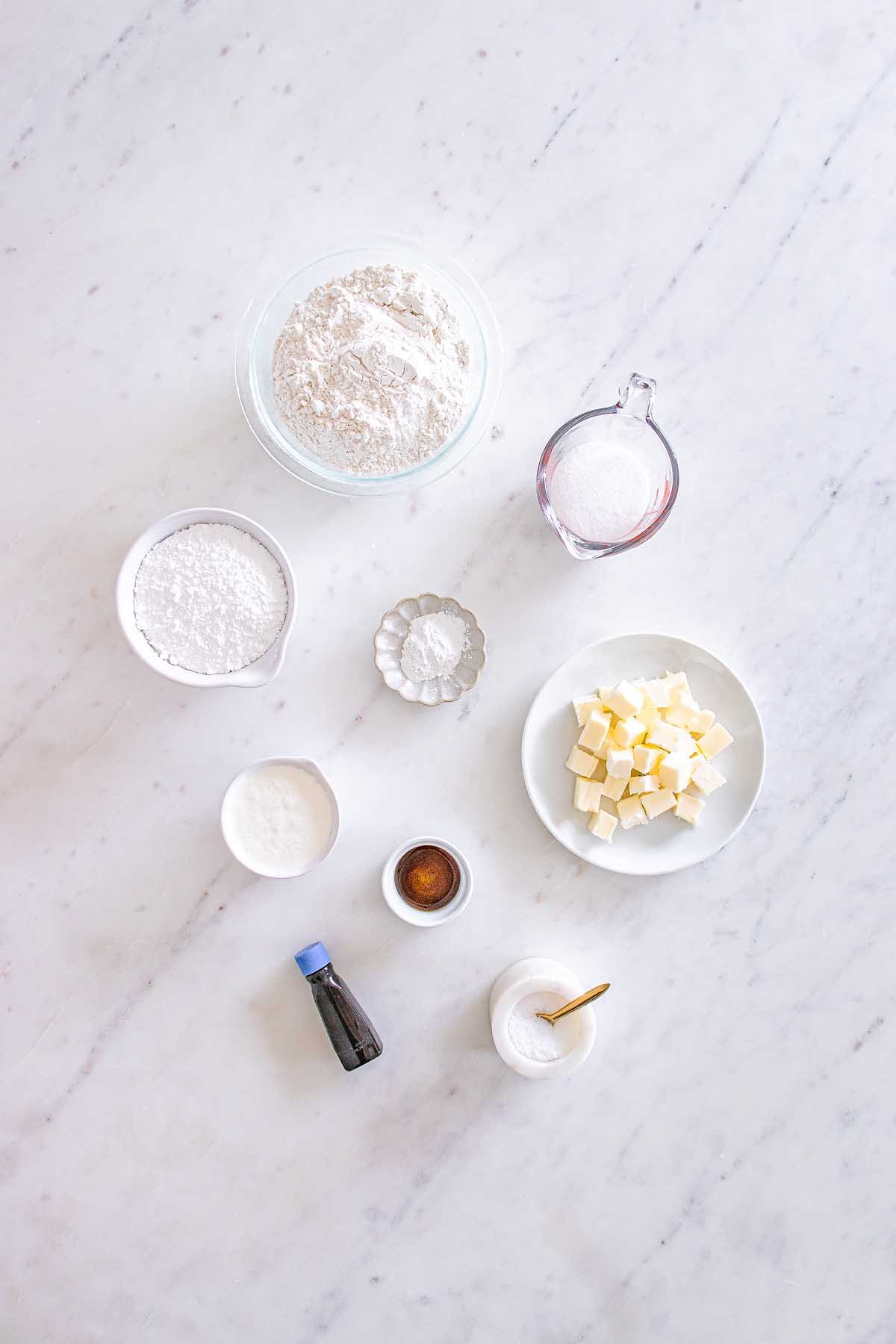 Baking ingredients on a marble surface: flour, sugar, butter cubes, vanilla, salt, and powders in bowls—perfect for making Starbucks Copycat Vanilla Bean Scones.