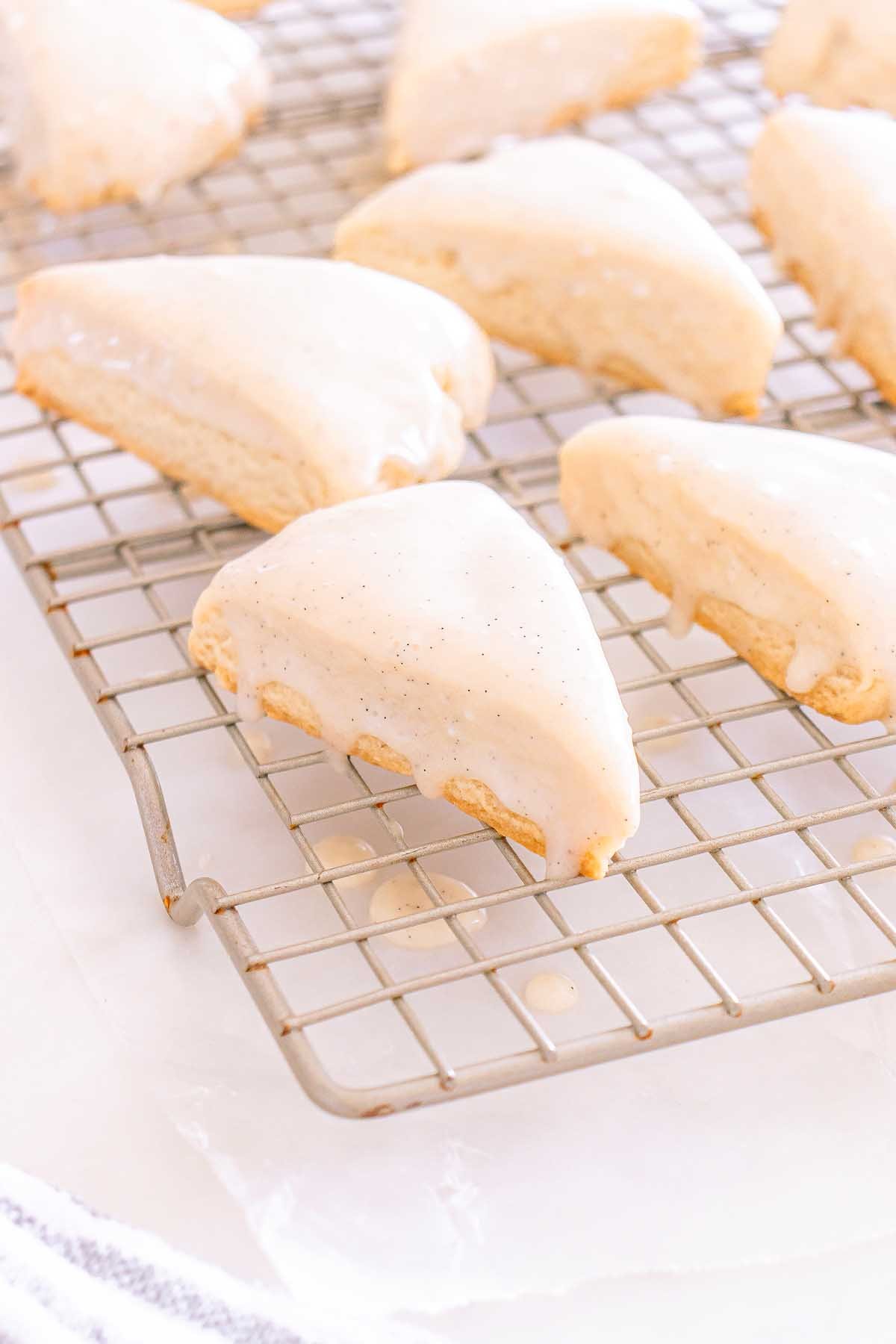 Starbucks Copycat Vanilla Bean Scones, shaped into triangles and topped with white glaze, cool on a rack as icing gently drips onto the surface below.