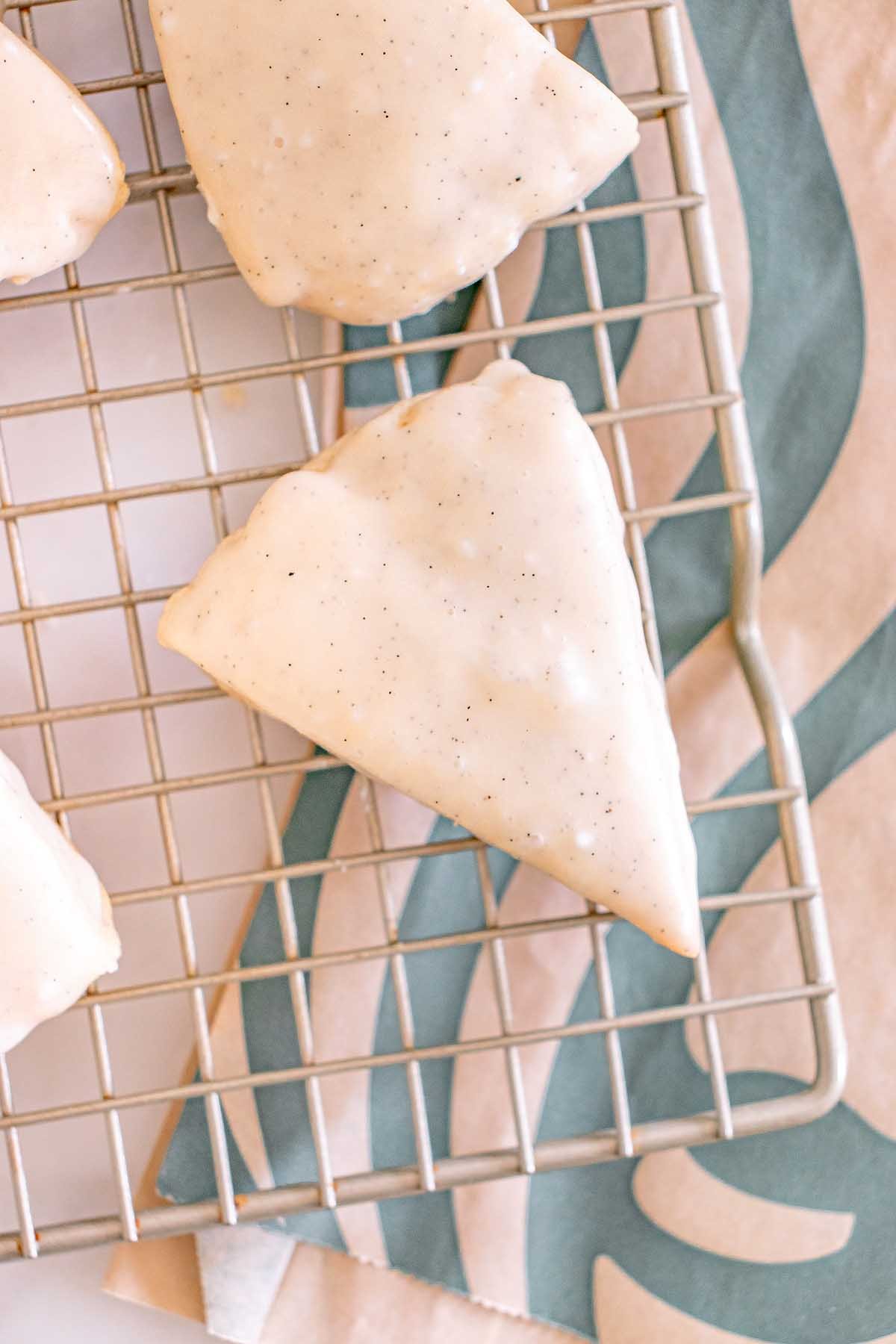 Starbucks Copycat Vanilla Bean Scone, iced and triangular, rests on a cooling rack with a patterned cloth underneath.