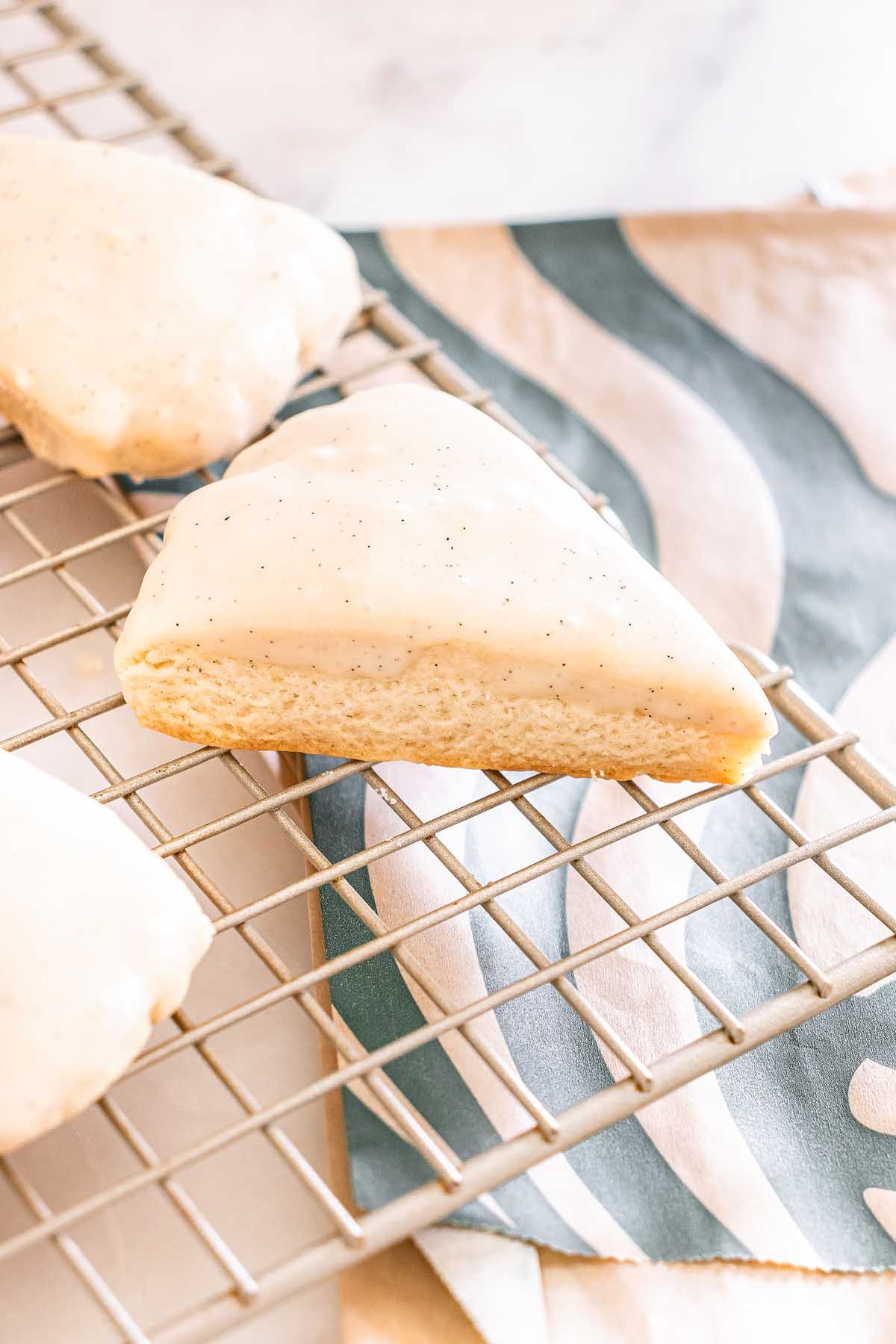 A Starbucks Copycat Vanilla Bean Scone rests on a cooling rack, with a patterned napkin underneath.