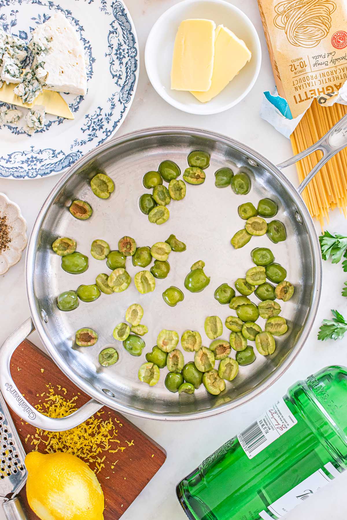 A pan with green beans, surrounded by butter, cheese, pasta, lemon, a box of San Pellegrino, and hints of dirty martini pasta inspiration.