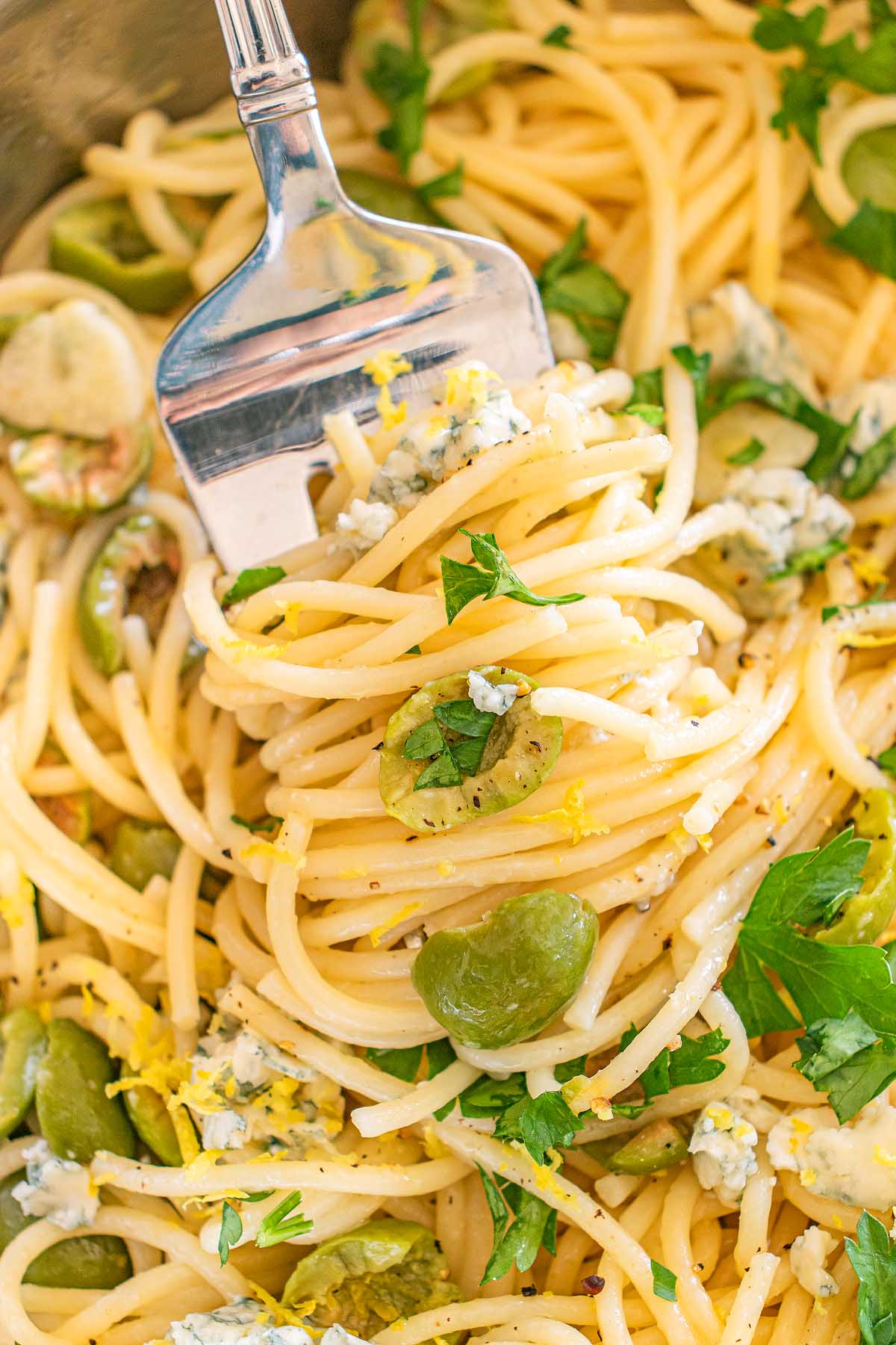 A fork twirls dirty martini pasta with green olives, parsley, and crumbled cheese.