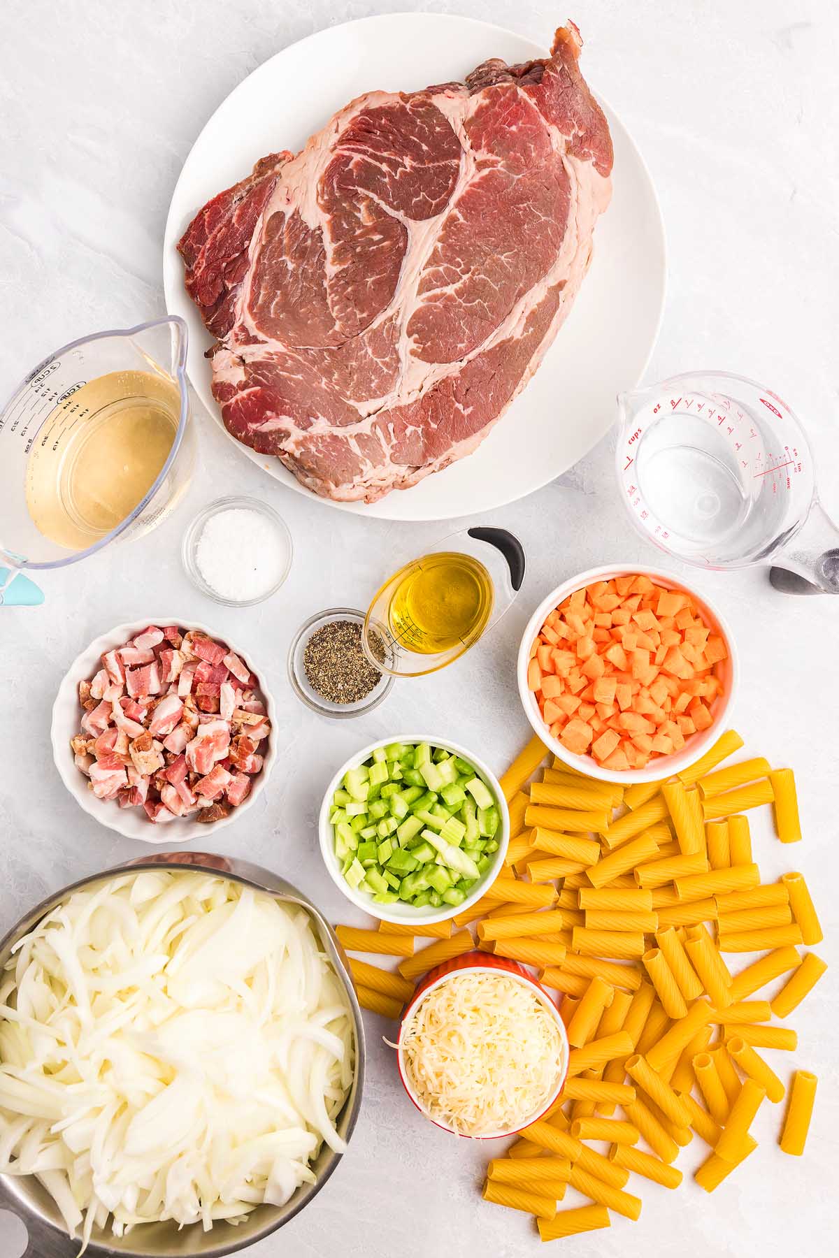 A hearty pasta alla Genovese dish featuring raw beef, rigatoni pasta, sliced onions, chopped bacon, celery, carrots, cheese, seasoning, broth, and olive oil.