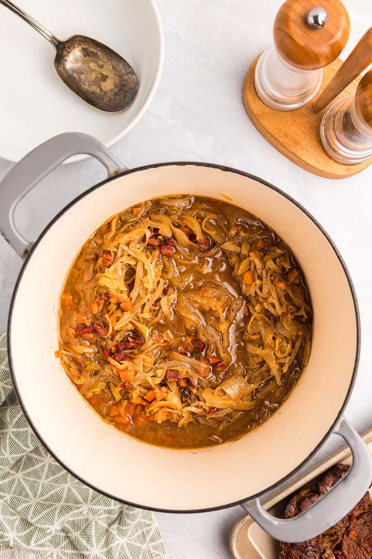 A pot of cooked onions, carrots, and gravy&mdash;reminiscent of pasta alla Genovese&mdash;sits on a countertop next to a spoon and salt and pepper shakers.