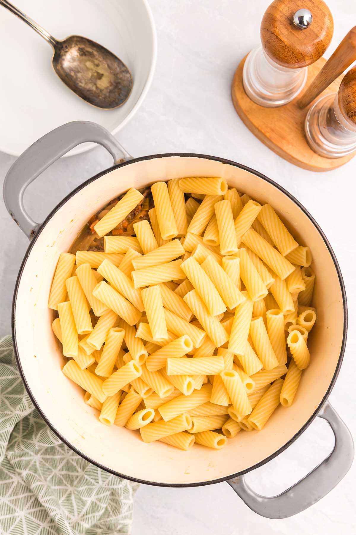 A white pot filled with cooked rigatoni pasta, perfect for making pasta alla Genovese, sits on a countertop beside salt and pepper shakers.