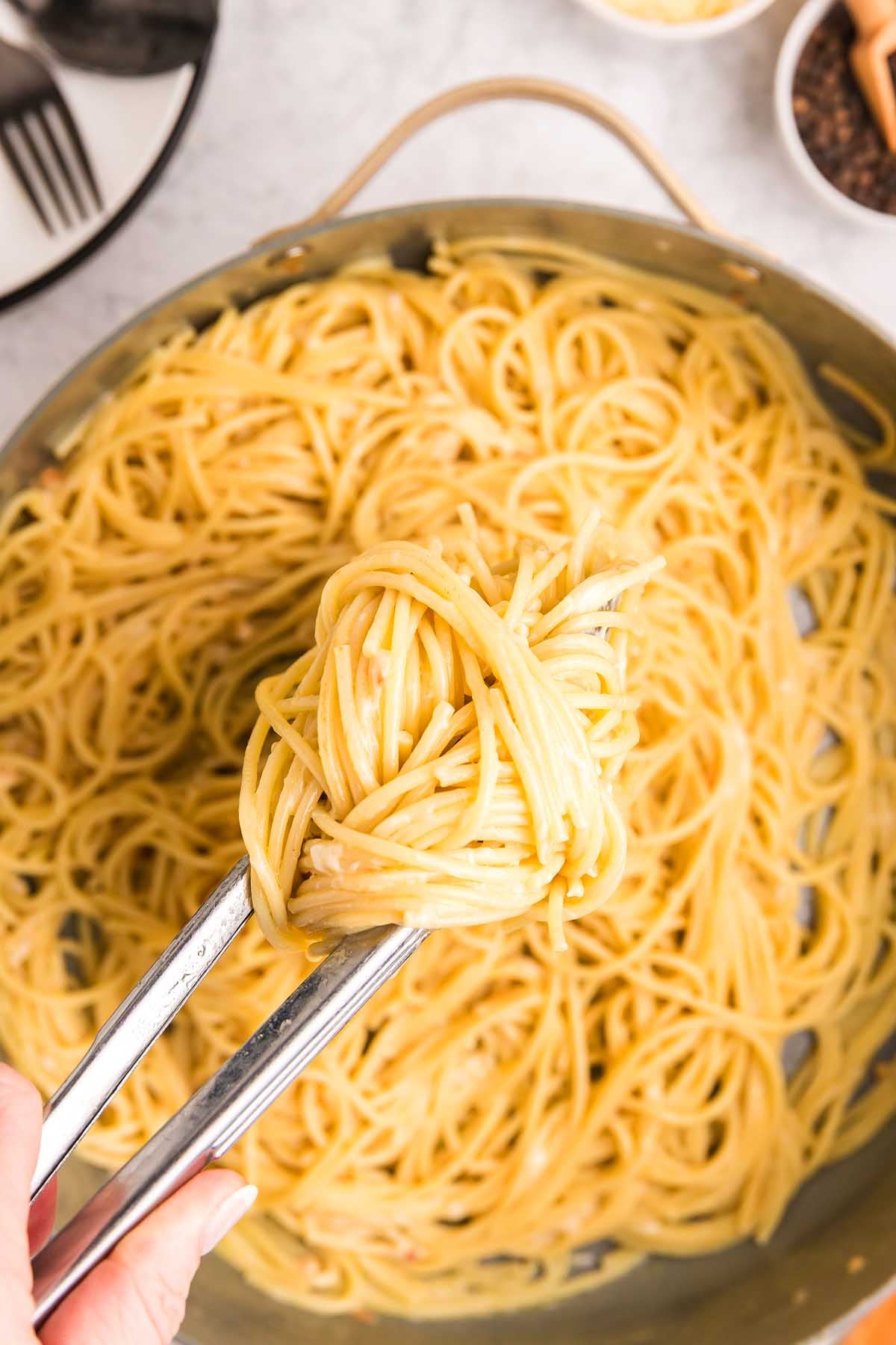 Tongs holding a portion of pasta alla Nerano above a pan filled with more spaghetti.