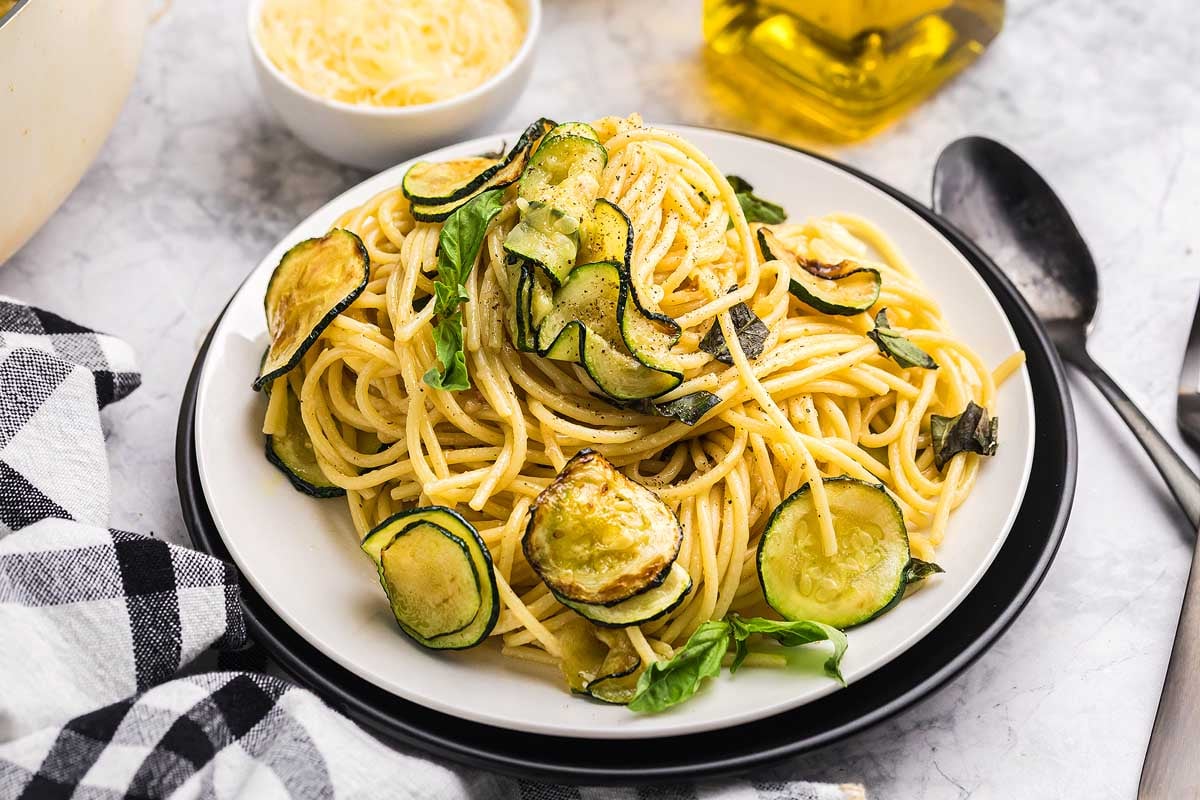 A plate of pasta alla Nerano featuring spaghetti with saut&eacute;ed zucchini and fresh basil, served with a fork on the side.
