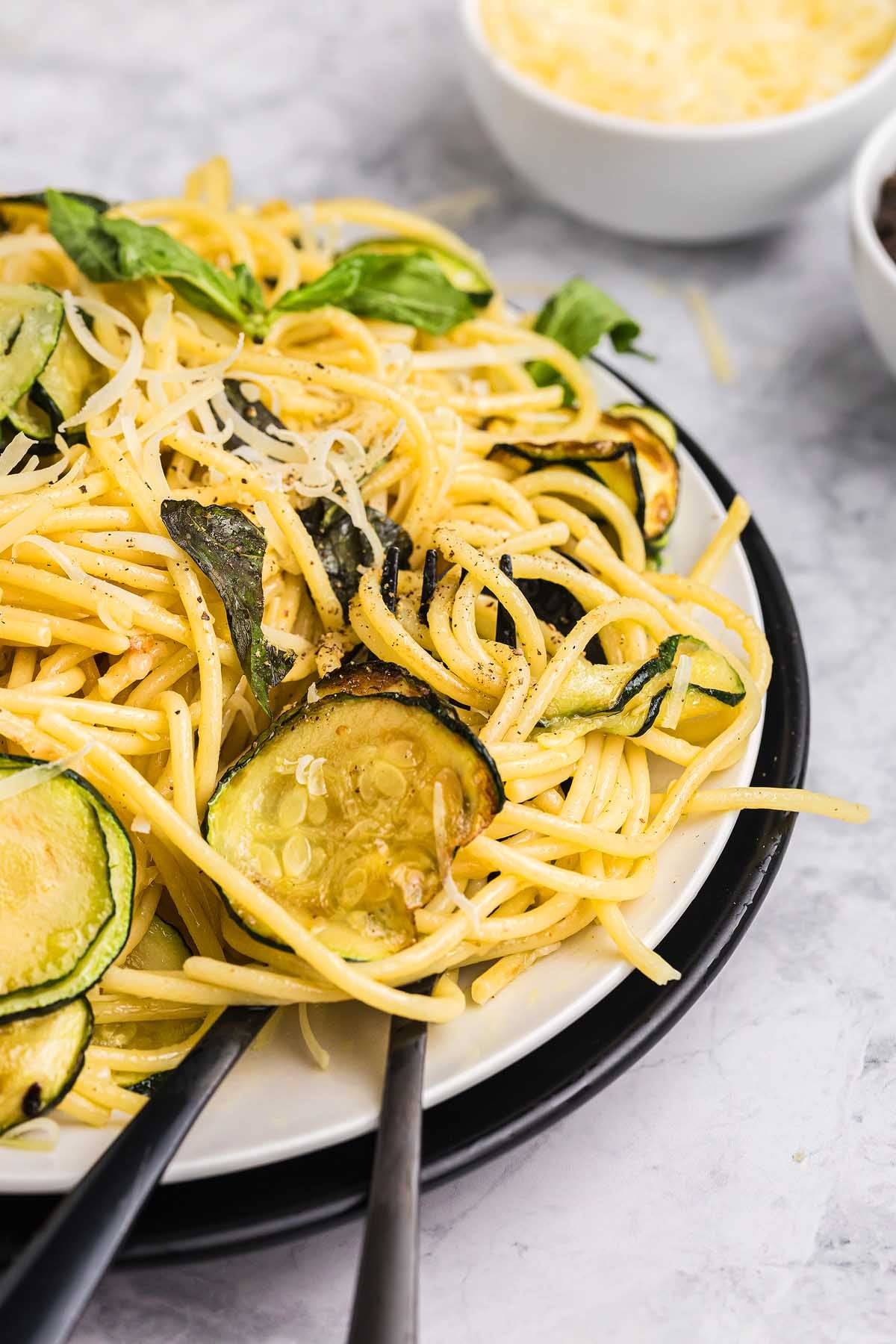 A plate of pasta alla Nerano featuring spaghetti with zucchini, fresh basil, and grated cheese, served with a fork and spoon.