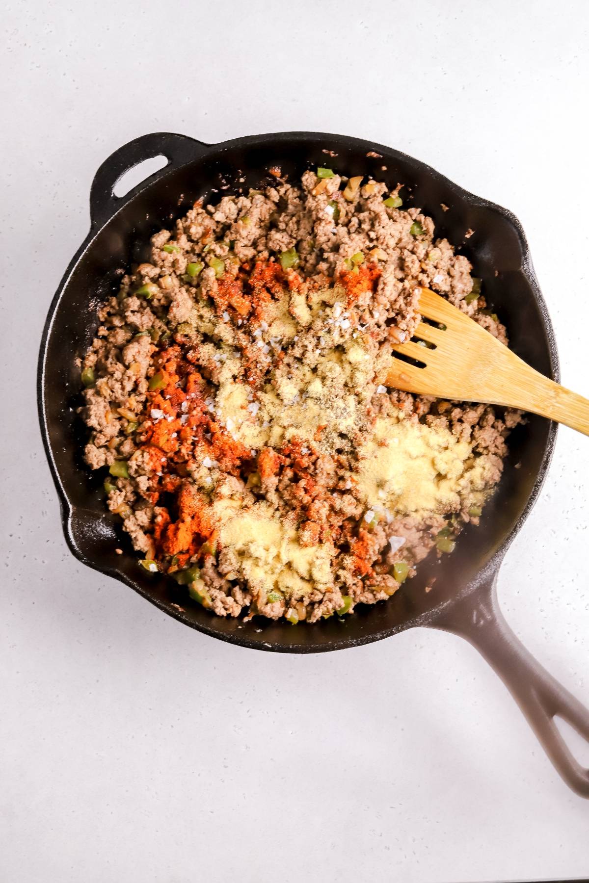 Ground beef and diced vegetables sizzle in a cast iron skillet with spices, stirred with a wooden spatula—perfect for filling your air fryer beef taquitos or trying in the best air fryer recipe.