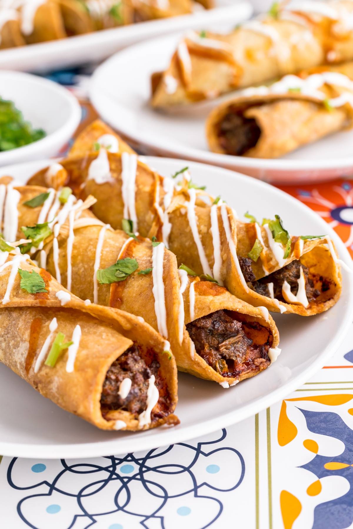 Three crispy air fryer beef taquitos drizzled with white sauce and garnished with cilantro on a white plate—a Gluten free Mexican dinner that's both delicious and easy to make.