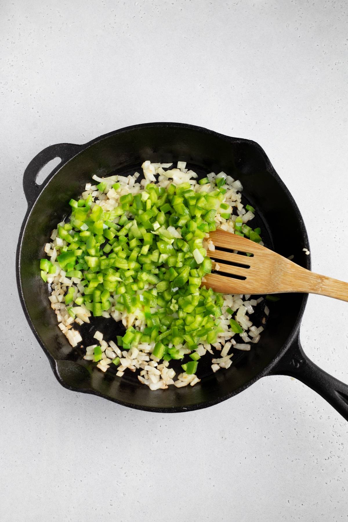 Diced onions and green bell peppers being sautéed in a black skillet with a wooden spatula, perfect as a flavorful base for the best air fryer recipe like air fryer beef taquitos.