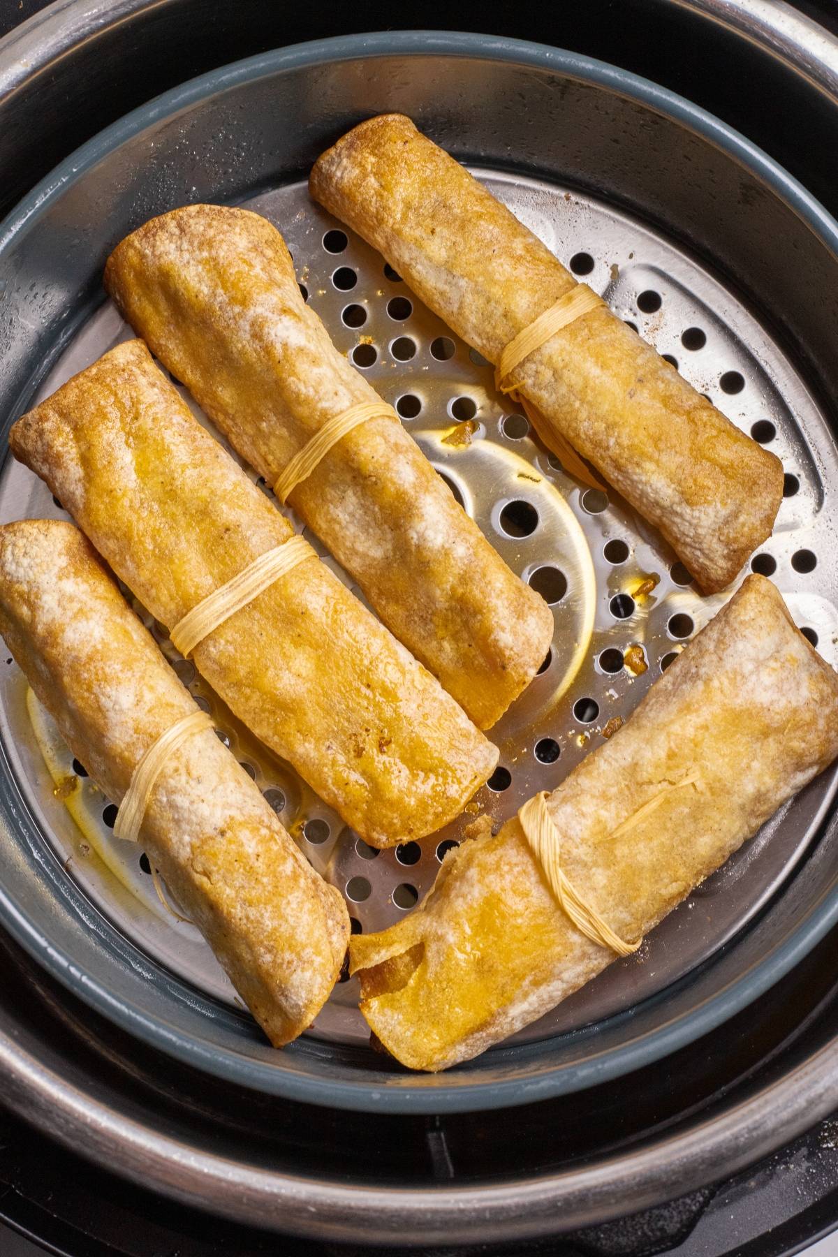 Five golden-brown bean curd rolls tied with strips, steaming in a round metal steamer tray—these could easily be the next best air fryer recipe for those seeking healthy and delicious alternatives.