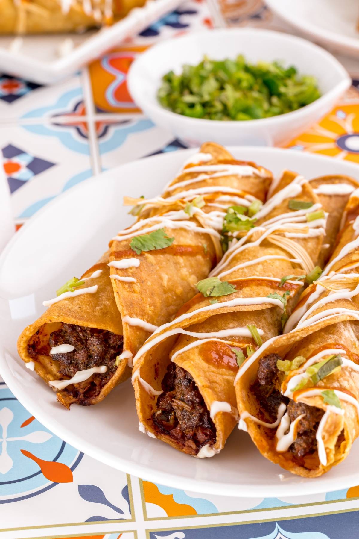 Three crispy air fryer beef taquitos drizzled with crema and garnished with cilantro, served on a white plate—a delicious gluten free Mexican dinner option.