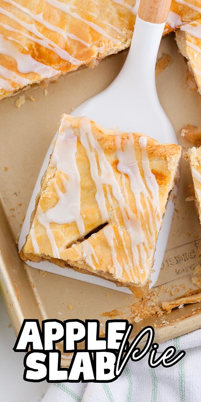 A slice of apple slab pie, its golden crust gleaming with glaze, is being lifted from a baking pan with a white spatula.