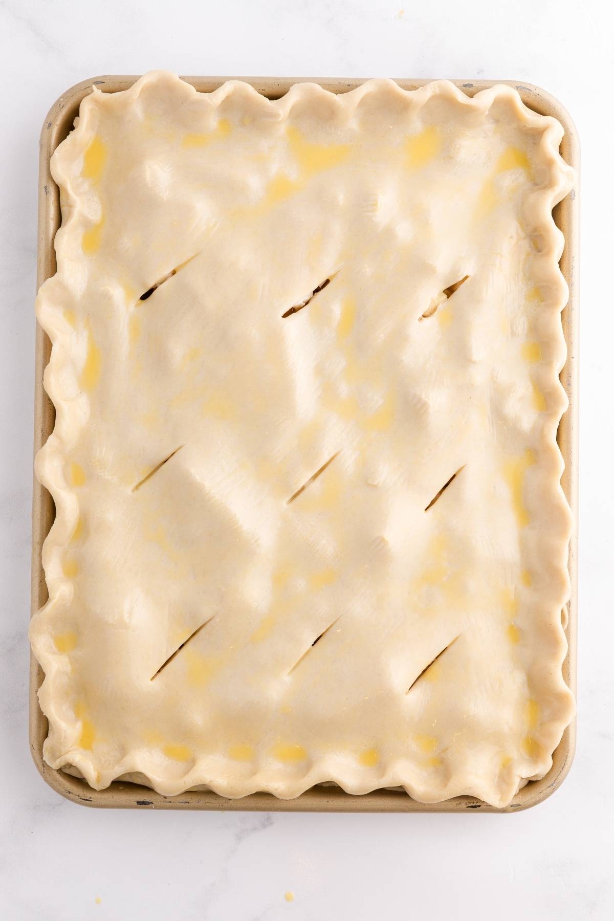 Unbaked rectangular pie with a crimped edge and several slits in the top crust, on a baking sheet.
