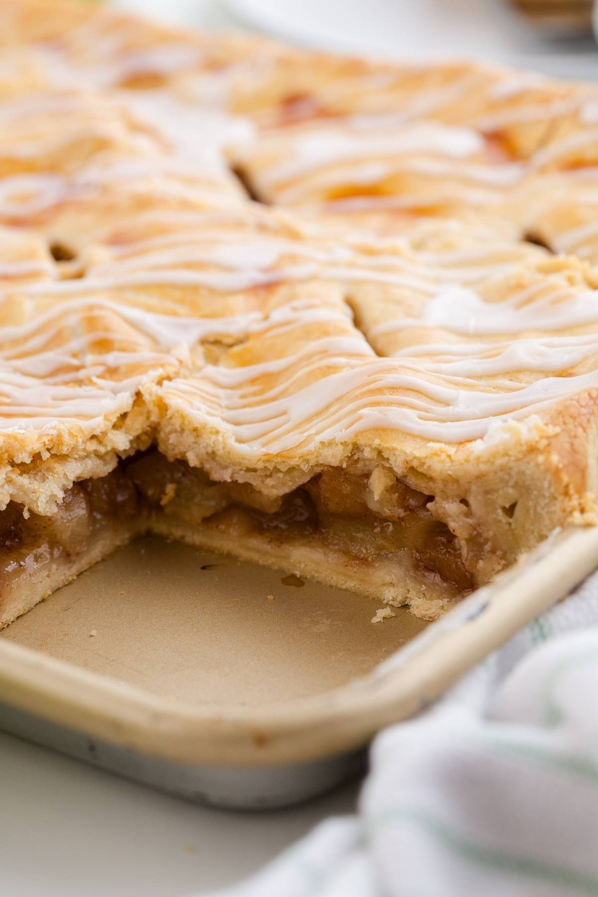 A close-up of a glazed apple slab pie with a piece missing, showing the apple filling inside.