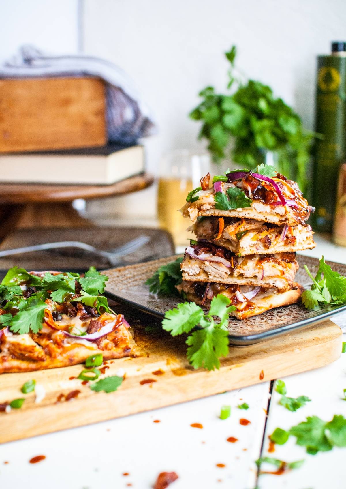 Stacked slices of BBQ Chicken Flatbread Pizzas topped with red onions, cilantro, and melted cheese on a table—an easy way to make flatbread pizza at home.