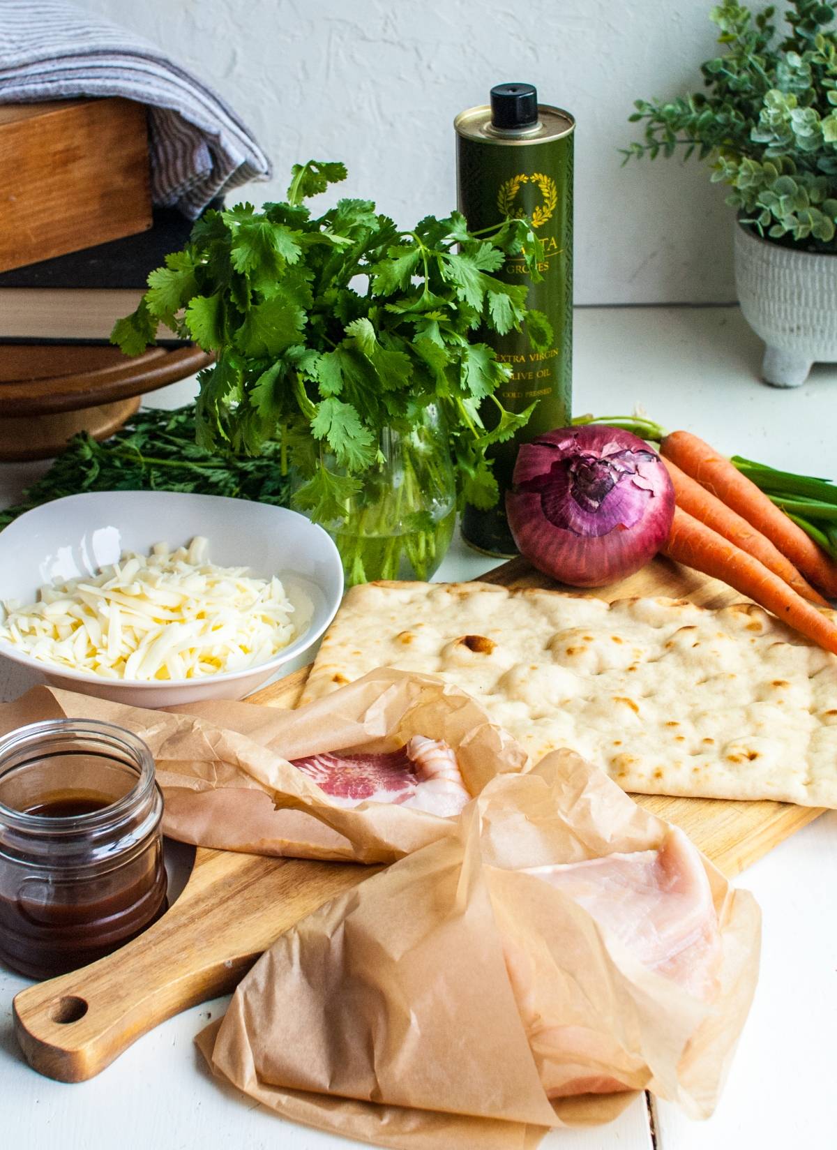 Flatbread, raw fish, shredded cheese, red onion, carrots, cilantro, oil, and sauce on a wooden board—ideal inspiration if you want to make flatbread pizza at home.