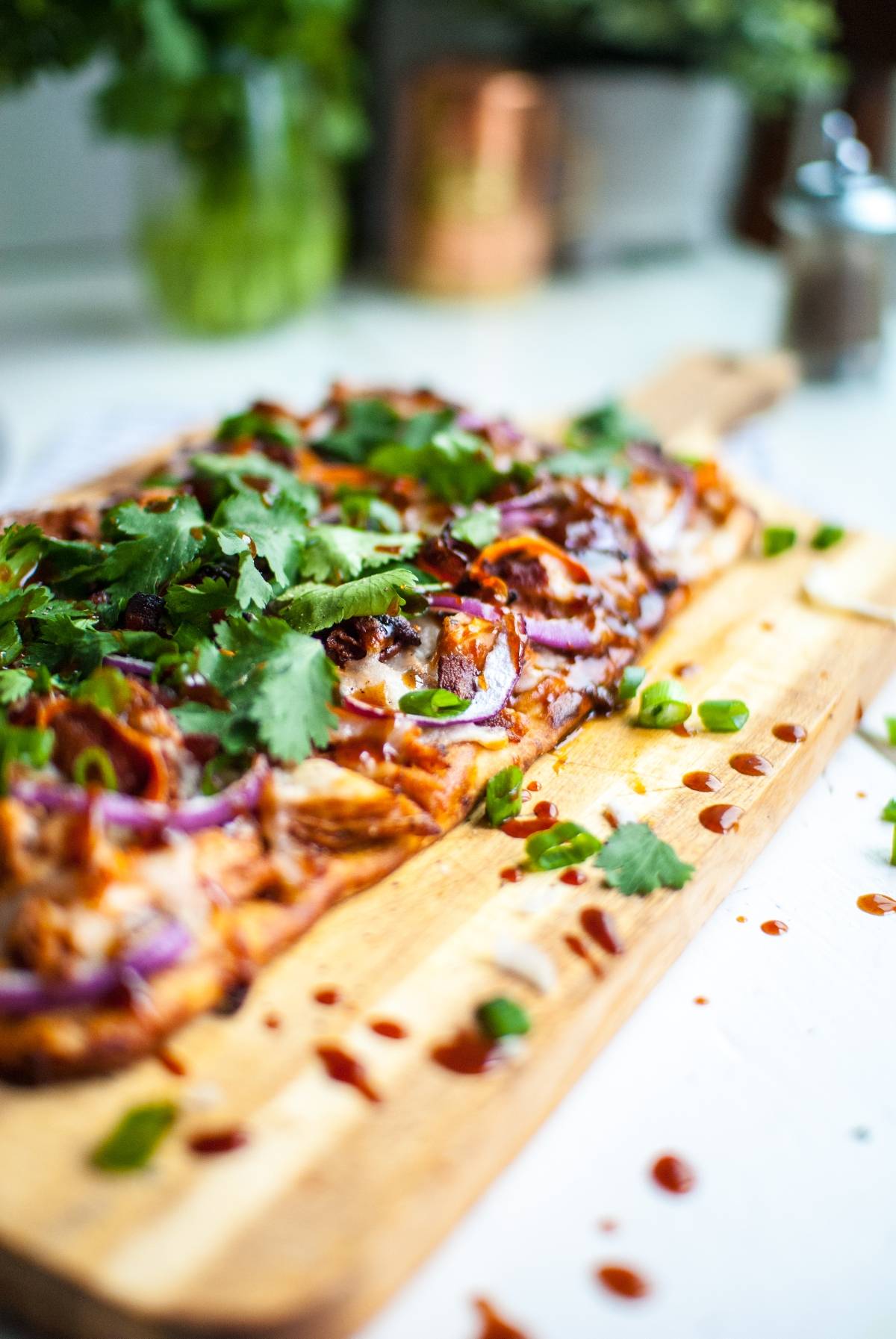 Flatbread topped with chicken, red onions, green onions, cilantro, and sauce on a wooden board—just like a BBQ Chicken Flatbread Pizza from Panera.