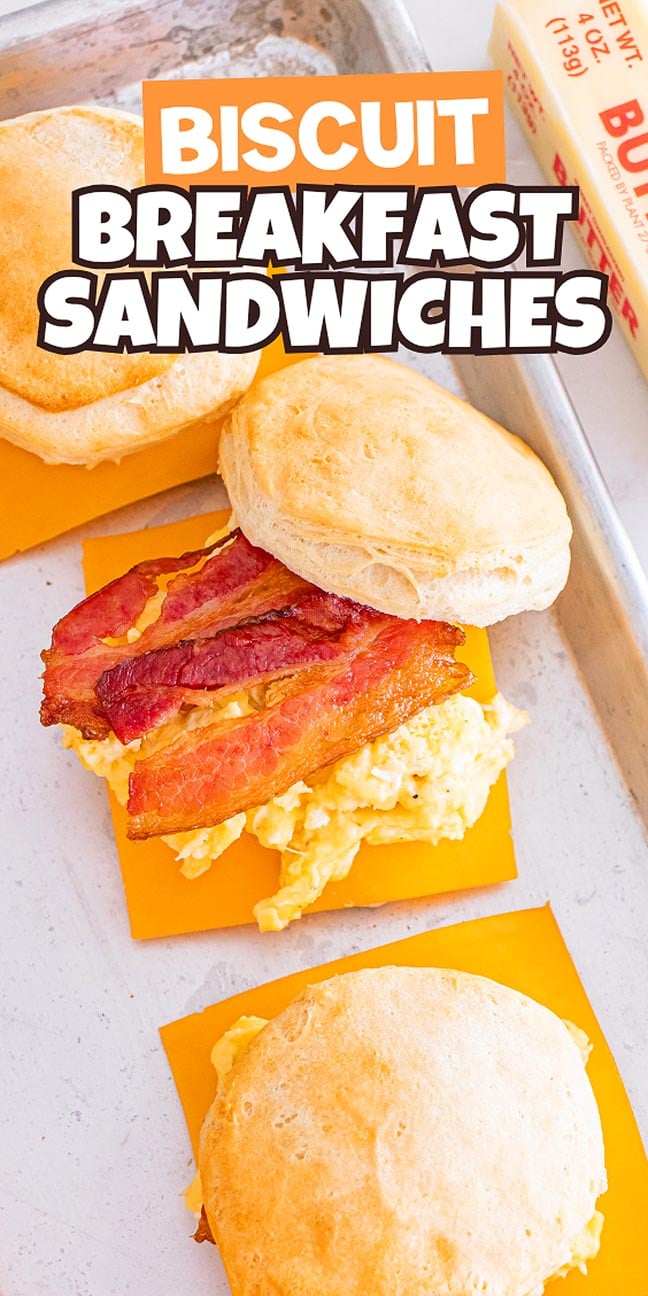 Three biscuit breakfast sandwiches with scrambled eggs, cheddar cheese, and bacon served on a light tray.