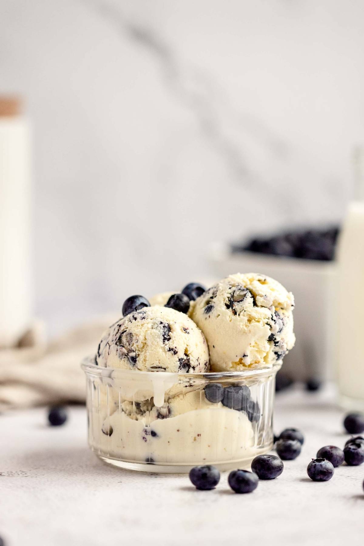 Three scoops of Blueberry Cheesecake Ice Cream in a glass bowl, garnished with fresh blueberries—a delicious twist on classic blueberry ice cream.