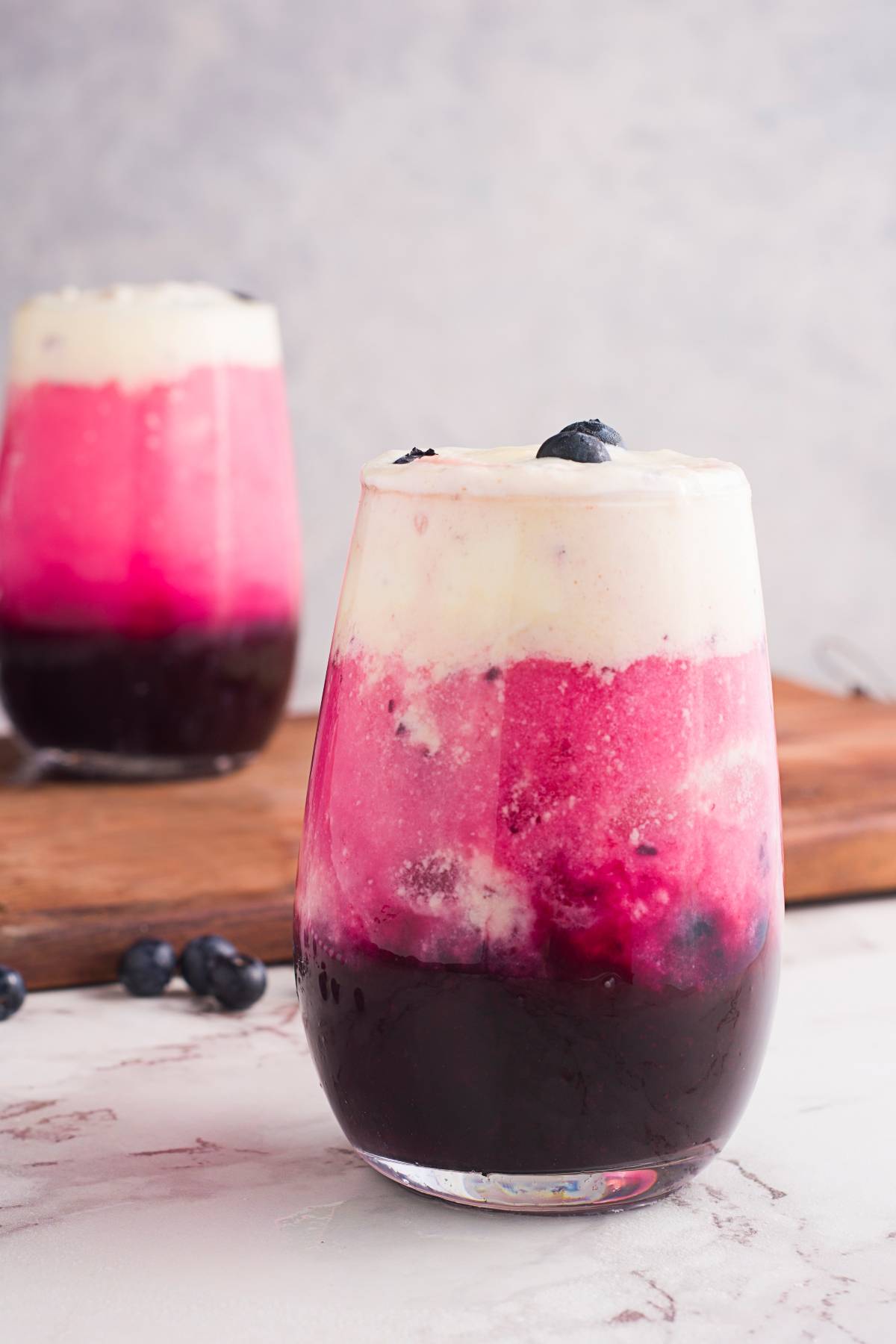 Layered sparkling blueberry float in a clear glass, garnished with blueberries, on a marble surface—a fresh blueberry recipe perfect for summer refreshment.