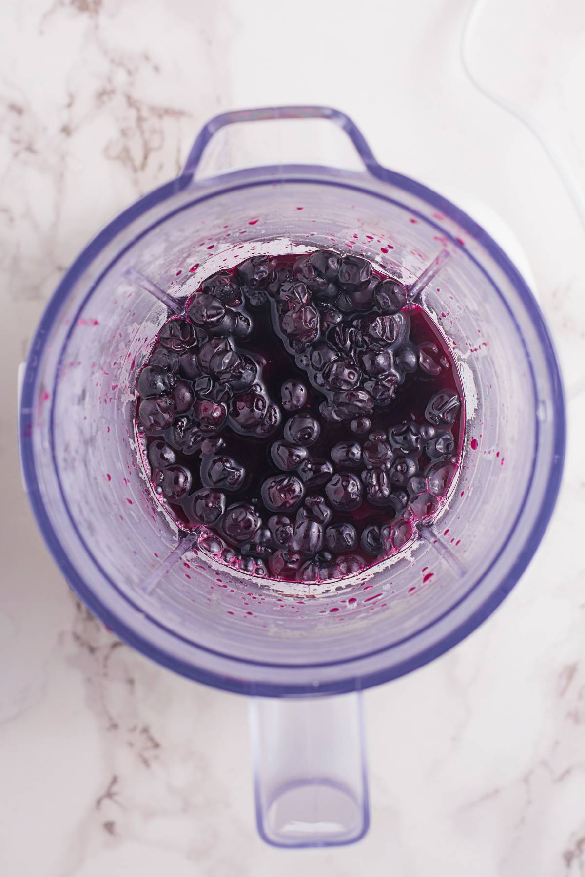 Overhead view of fresh blueberries and juice in a blender on a marble countertop, perfect for creating a refreshing sparkling blueberry float or another delicious fresh blueberry recipe.