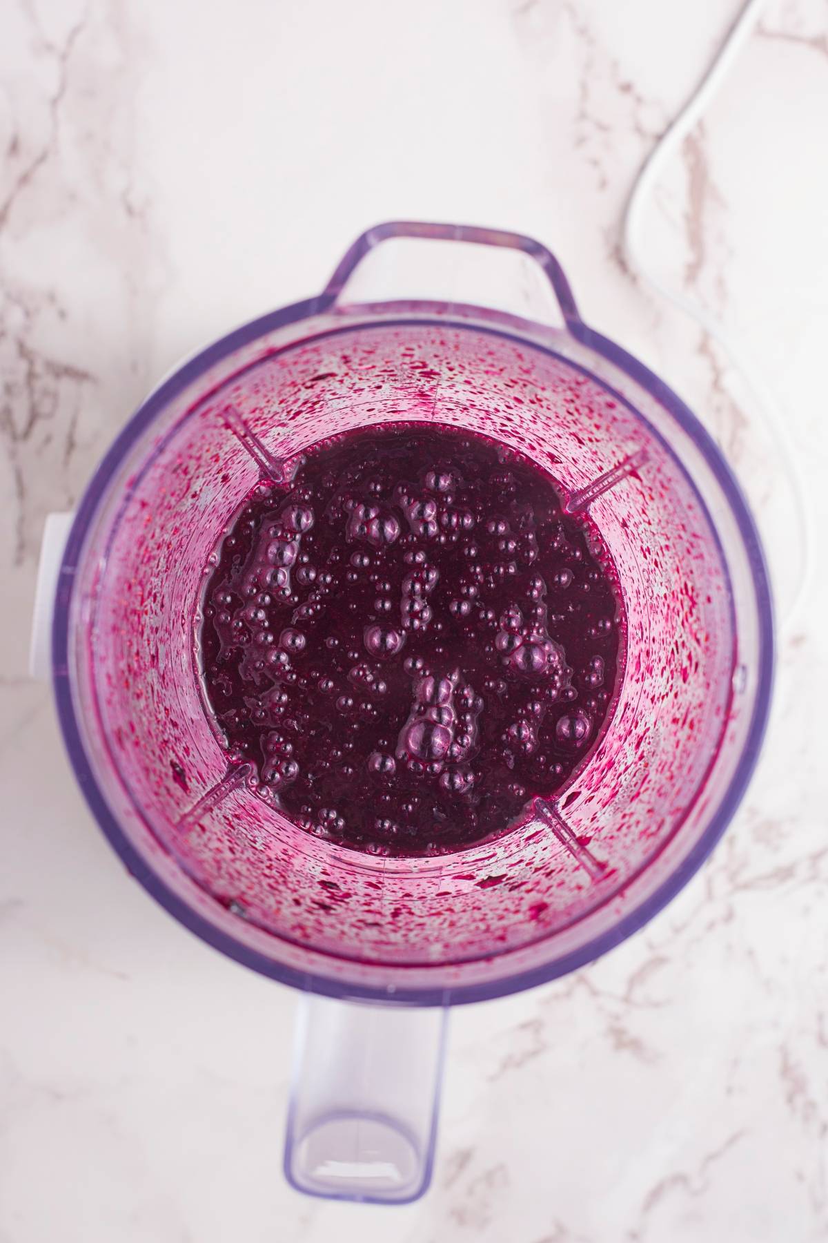 Top view of a blender containing a thick, dark purple liquid mixture with bubbles on the surface, perfect for creating a blueberry ice cream float or trying out a fresh blueberry recipe.