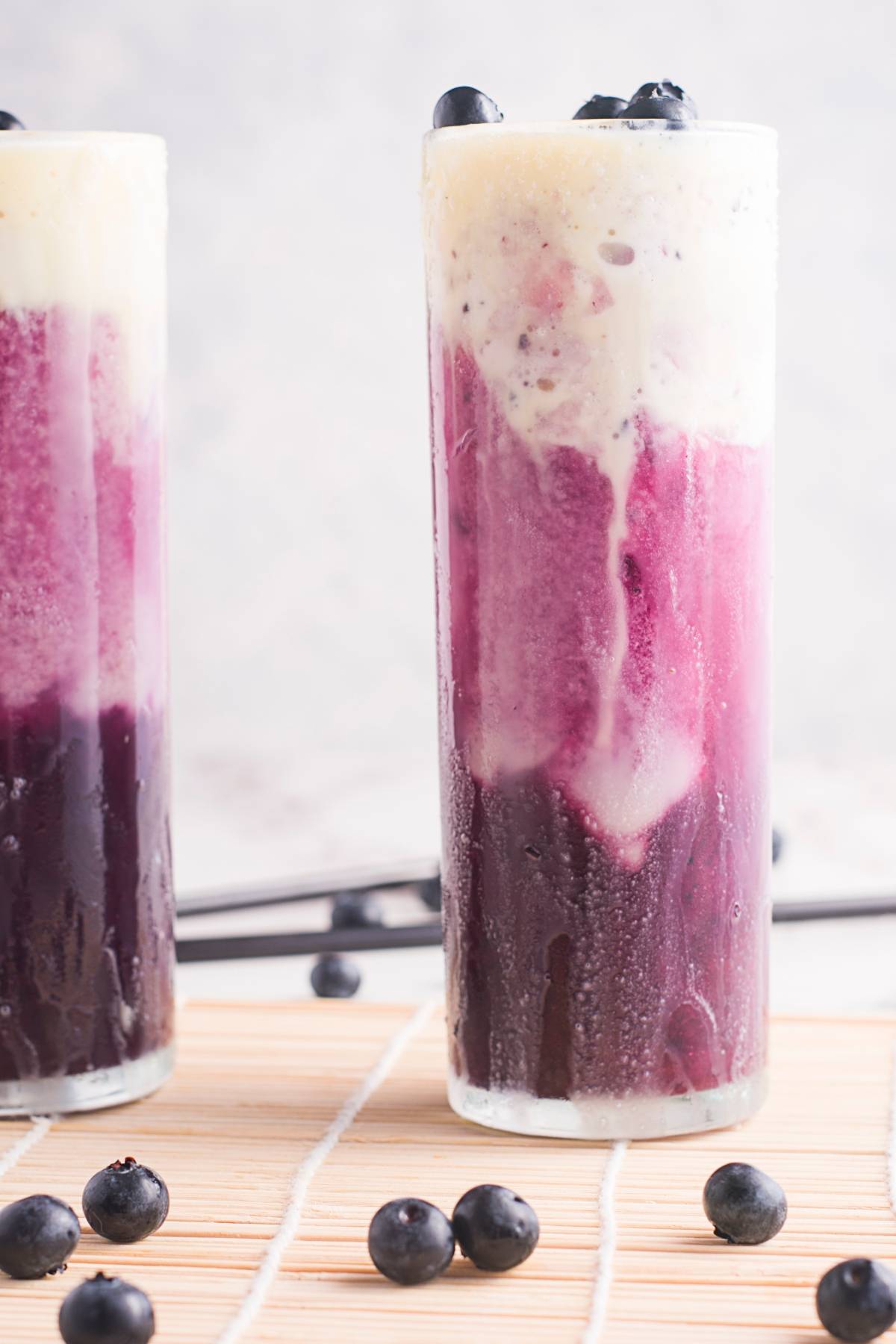 Tall glass with a layered purple and white Sparkling blueberry float, topped with blueberries; fresh blueberries beside the glass.