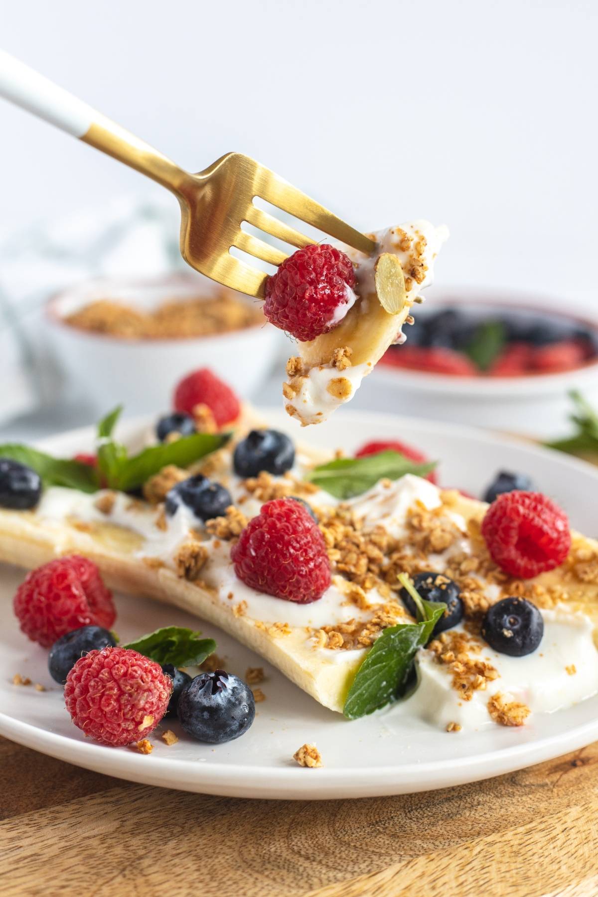 A fork holds yogurt, berries, and granola above a plate of banana, berries, granola, and yogurt—a fun alternative to a smoothie bowl and one of the best healthy breakfast ideas for kids.