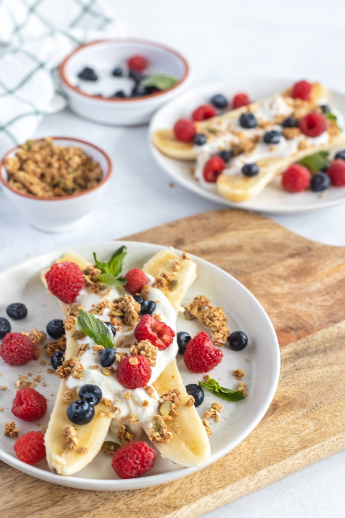 Sliced banana and fresh berries topped with yogurt, granola, and mint on white plates—an easy alternative to a smoothie bowl and one of the best healthy breakfast ideas for kids.