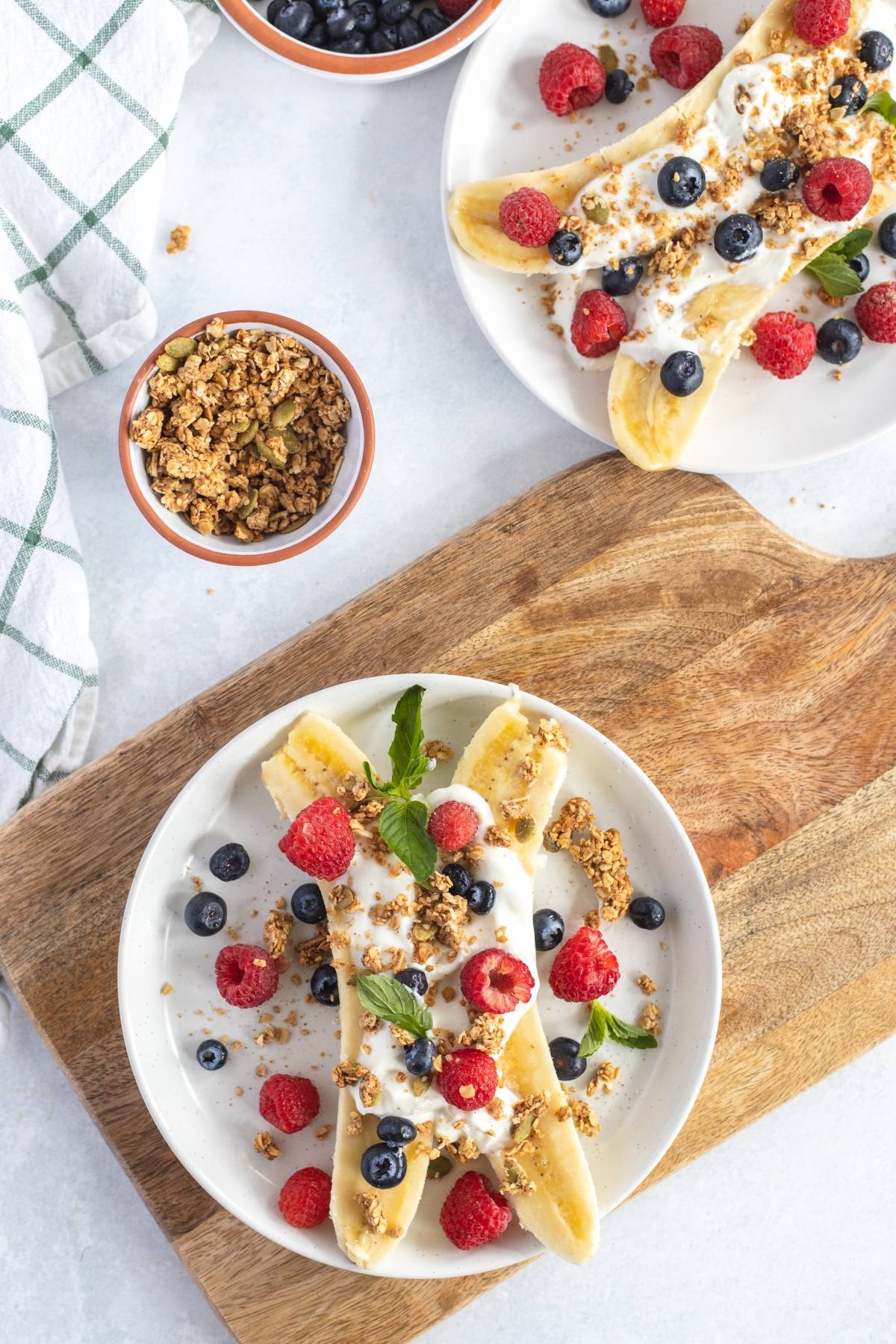 Breakfast Banana Split topped with yogurt, granola, raspberries, blueberries, and mint on white plates—an easy no cook breakfast and one of the best healthy breakfast ideas for kids.