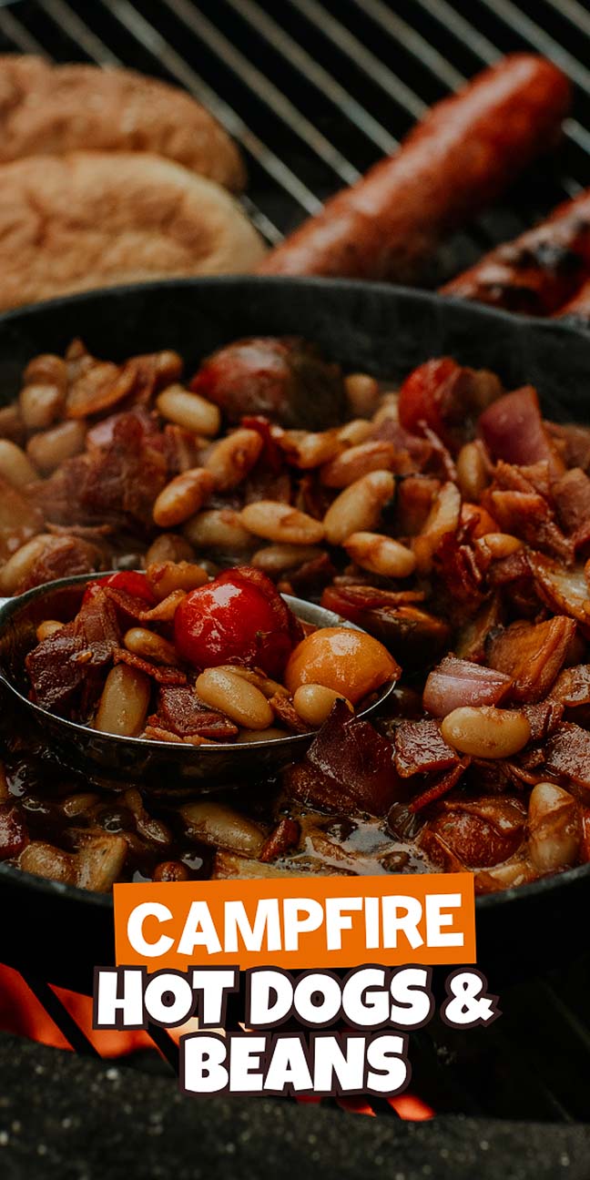 A cast iron skillet of campfire hot dogs and beans cooking over a campfire grill, with text "Campfire Hot Dogs & Beans.