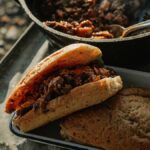 Campfire sloppy joes served on a tray, filled with savory meat and sauce, accompanied by a pot of stew and another piece of bread nearby.