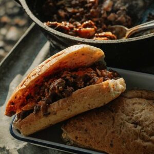 Campfire sloppy joes served on a tray, filled with savory meat and sauce, accompanied by a pot of stew and another piece of bread nearby.
