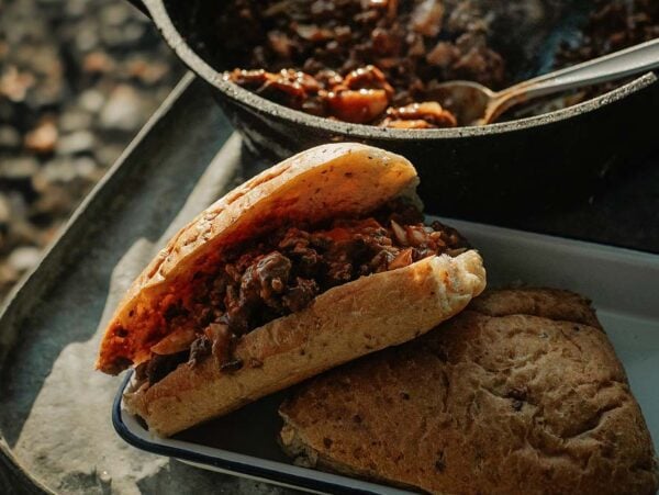 Campfire sloppy joes served on a tray, filled with savory meat and sauce, accompanied by a pot of stew and another piece of bread nearby.